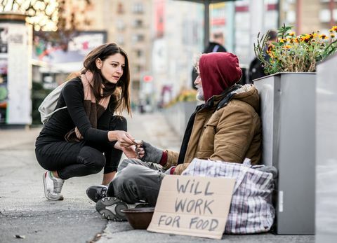 Jauna moteris duoda pinigų benamiui elgetaujančiam vyrui, sėdinčiam mieste.