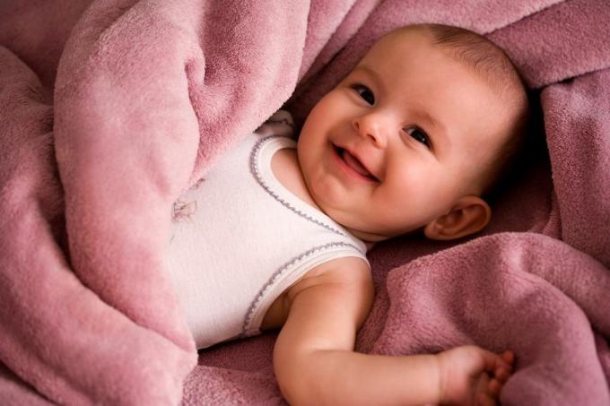 besišypsančio kūdikio portretas baltais tanko stiliaus marškiniais, apvyniotas švelniai rožine antklode