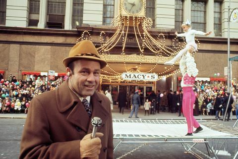 Joe Garagiola kalba į mikrofoną su akrobatais fone per Macy padėkos dienos paradą 1970 m.