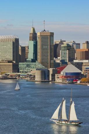 Baltimore panorama ir vidinis uostas su trimis burlaiviu ant vandens priekiniame plane ir dviem burinėmis valtimis fone