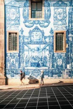 moteris, vaikštanti Porto prie mėlynos ir baltos azulejos plytelių sienos iš Capela das almas bažnyčios Porto