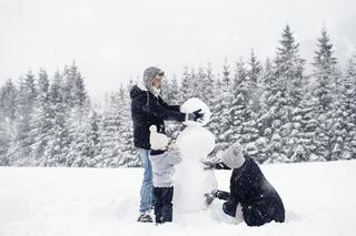 trijų asmenų šeima sniege stato sniegą