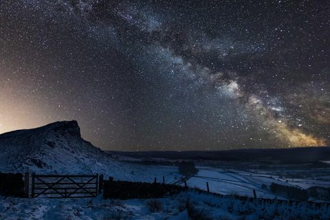 Ryškus Pieno kelio kompozicinis vaizdas virš sniegu padengto Peak District nacionalinio parko kraštovaizdžio Anglijoje