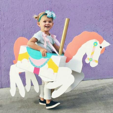 maža mergaitė su dėžute, kurios forma ir dažai yra panašūs į karuselinį žirgą