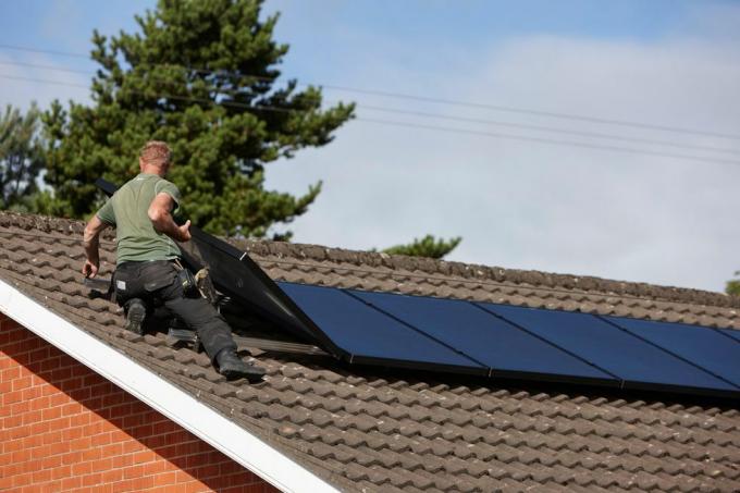 h0chn1 vyras, montuojantis ant stogo saulės kolektorių masyvą vietiniame saulės kolektorių įrengime JK