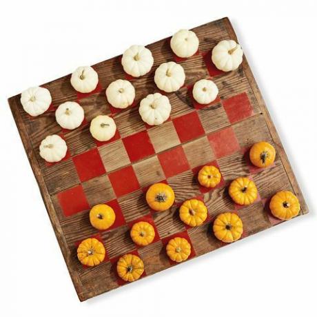 medinė lenta, nudažyta kaip šaškių žaidimas, o žaisme naudojami balti ir oranžiniai mini moliūgai