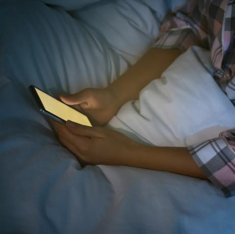 moteris, naktį lovoje naudojanti išmanųjį telefoną, nomofobija iš arti ir miego sutrikimo problema