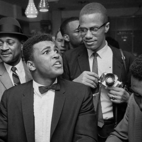 Majamio 1964 m. kovo mėn. juodas musulmonų lyderis malcolmas x 2r, erzinančiai atsirėmęs į tuxo plakiruoto kasio molio petį, dabar muhammadas ali l, kuris savavališkai sėdi prie soda fontano, apsuptas džiūgaujančių gerbėjų po to, kai jis įveikė Sonny Listoną sunkiasvorio pasaulio čempionato nuotraukoje, kurią pateikė Bobas Gomelas „Life images“ kolekcija per „Getty Images“