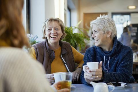 lesbiečių pora ir suaugusi dukra geria kavą ir kalbasi kavinėje