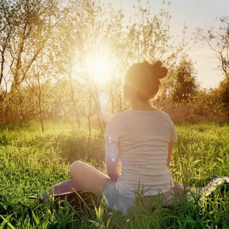 jauna moteris, sėdinti jogos pozoje, besimėgaujanti saulėlydžiu gamtoje