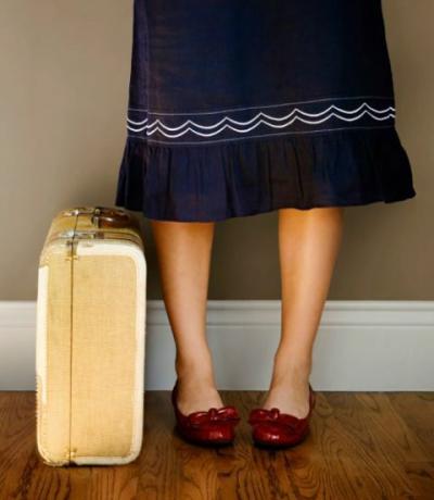 moteris mėlynu sijonu ir rubinais batais su lagaminu