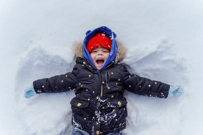 mažas vaikas sniege gamina sniego angelą