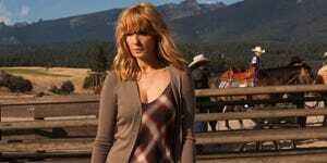 Kelly Reilly kaip Beth Dutton ruda balta ir raudona languota suknele su rudu megztiniu stovi priešais arklio aptvarą